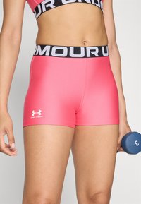 Rosa åtsittande träningsshorts med en svart elastisk midja som har vit text "UNDER ARMOUR"; slät yta och logotyp på vänster underkant.