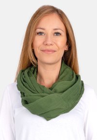 Grüner, strukturierter Schal, der in Schichten angeordnet ist und aus leichtem Material gefertigt ist. Locker um den Hals getragen, ergänzt er ein weißes Oberteil.