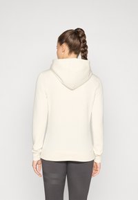 Sweatshirt cu glugă în bej deschis, cu o textură moale, mâneci lungi și o croială lejeră. Dispune de un buzunar tip cangur și de manșete ribbate.