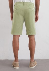 Light green cotton shorts with back pockets, a smooth texture, and a tailored fit, paired with beige shoes and simple styling.