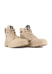 Botas de tobillo beige con una superficie texturizada, puntera redondeada, cordones y suela de goma con un patrón de relieve. Acentos negros y amarillos en los laterales.
