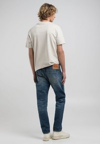 Ljusgrå bomullströja med klassisk rundad halsringning, i kombination med blå denimjeans; anmärkningsvärd läderflik på midjan.