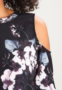 Blusa de hombros descubiertos con un estampado floral oscuro con flores blancas y moradas. Tejido ligero con una textura suave. Fondo negro.