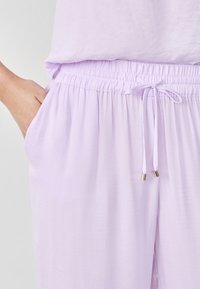 Lichtpaarse lichtgewicht broek met een elastische tailleband, een verstelbare trekkoord en zijzakken, gemaakt van een zachte, gestructureerde stof.