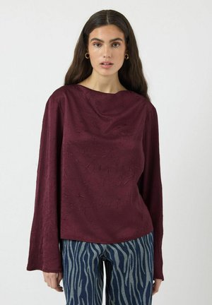 Burgundyröd topp med en strukturerad yta, bred båtkrage och långa klockärmar, kombinerad med blå och vita randiga jeans.