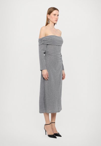 Rochie midi gri, fără umeri, cu mâneci lungi, textură cu caneluri și detalii plisate pe lateral, asortată cu tocuri stiletto negre elegante.