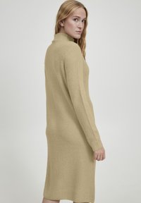 Beige, geribbelde gebreide jurk met een hoge kraag, lange mouwen en een rechte silhouet, tot halverwege de kuit reikend, met een gestructureerde afwerking.