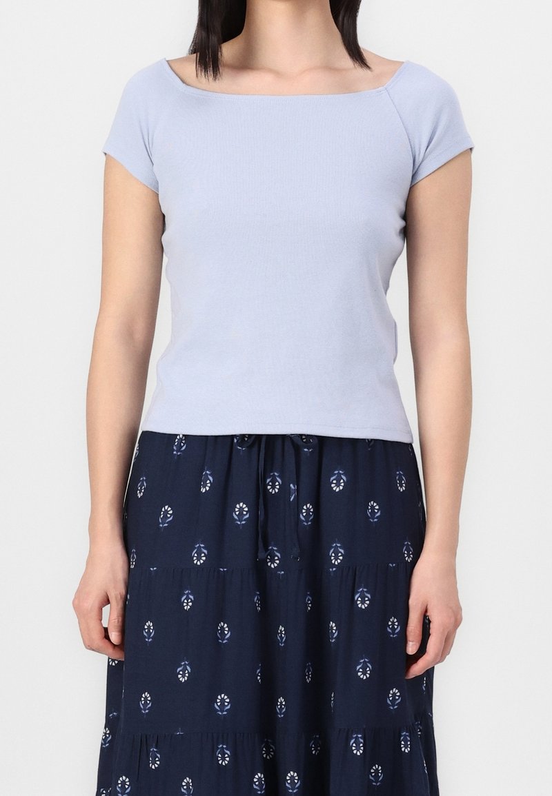 Femme portant un haut ajusté à manches courtes bleu clair et une jupe bleu marine avec de petits motifs de feuilles blanches.