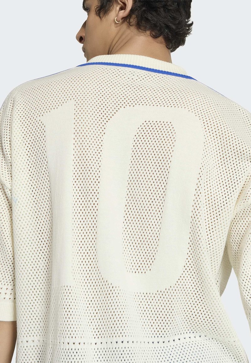 Man draagt een wit gaas-shirt met een groot nummer 10 op de achterkant en een kraag met blauwe rand, iets zijwaarts gedraaid.