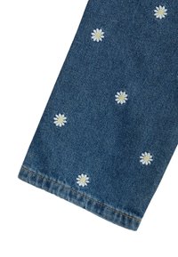 Tejido de mezclilla con bordados de margaritas blancas con centros amarillos, exhibiendo un color clásico de jeans azules, y un dobladillo recto con costuras visibles.