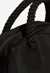 Černá látková taška s pletenými černými uchy, zapínáním na zip a texturovaným detailem popruhu nahoře. Kompaktní, funkční design.