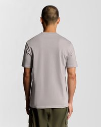 Svetlo siva kratka majica s kratkimi rokavi in okrolim ovratnikom, gladke teksture in običajnega kroja, v kombinaciji z olivno zelenimi cargo kratkimi hlačami.