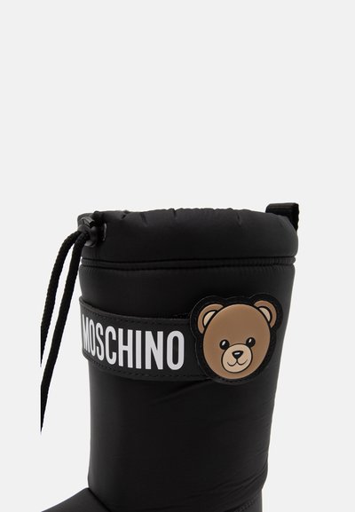 Μαύρη χειμερινή μπότα Moschino με κορδόνι στην κορυφή και λογότυπο προσώπου αρκούδας σε λουράκι πάνω στο επάνω μέρος της μπότας.