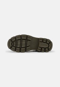 Suela de zapato de goma verde oscuro con profundos surcos y el nombre de la marca "Tamaris" con el número de talla 37 grabado en la sección del arco.