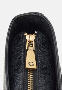 Mustan nahkalaukun sisäosa, jossa on kohopintakuosi, kultainen vetoketju, jossa on "G"-vetotappi, ja teksturoitu kangasvuori.