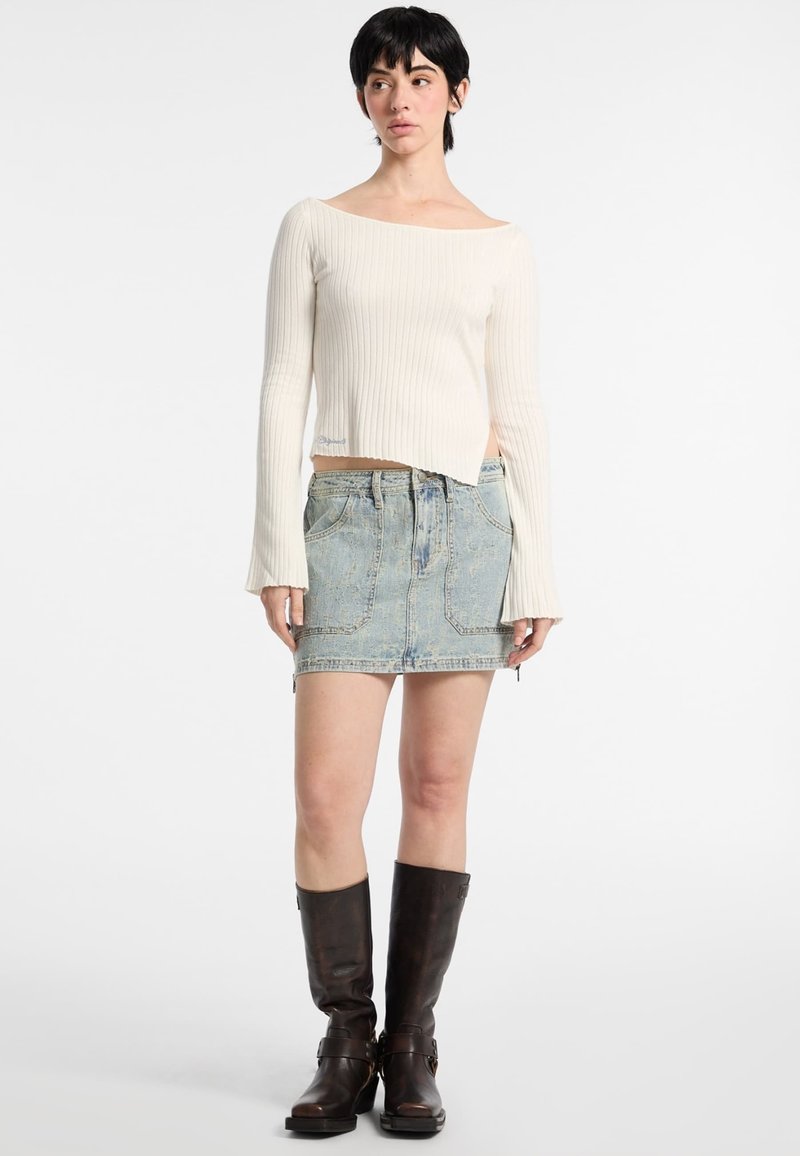 Maglione a spalle scoperte color crema a coste, mini gonna in denim azzurro con tasche frontali, stivali lunghi beige. I tessuti contrastano, abbigliamento casual.