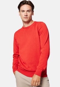 Czerwony sweter dzianinowy z okrągłym dekoltem, ściągaczami przy mankietach i dole, z małym logo z przodu. Gładka faktura i dopasowany krój.