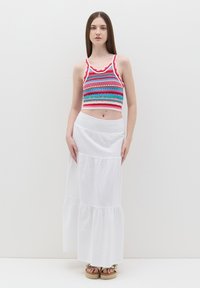 Top corto lavorato a maglia colorato con scollatura ondulata, abbinato a una gonna maxi bianca a strati. Presenta una vita arricciata per una vestibilità comoda.