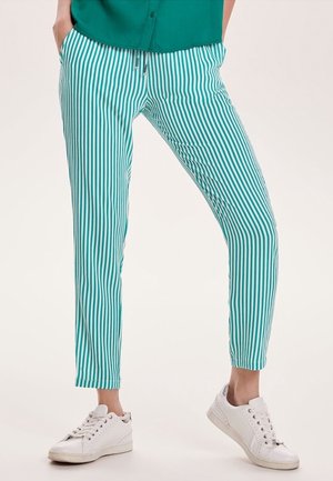 Pantalons rayés bleu-vert et blanc avec une coupe slim, dotés d'une taille à cordon de serrage et d'un tissu lisse, associés à des baskets blanches.