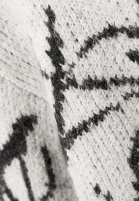 Kötött pulóver, amely fekete geometrikus mintázattal rendelkezik fehér háttéren, lágy textúrával, látható szálakkal és öltésekkel.