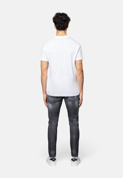 Witte t-shirt met korte mouwen in combinatie met donkere spijkerbroek, met een slim fit en een medium wash met versleten accenten. Sneakers maken de look compleet.
