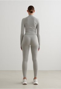 Top de manga larga gris y leggings ajustados hechos de una tela suave, con un cuello alto y un diseño sin costuras. Zapatillas blancas completan el look.