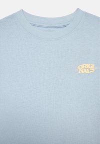 Světle modré bavlněné tričko s kulatým výstřihem. Obsahuje malé žluté logo s nápisem "ORIGINALS" a "1990" na levé části hrudi.