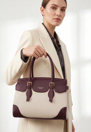 Donna con cappotto beige che tiene una borsa Diana&Co Firenze crema e viola scuro con doppie maniglie e dettagli con fibbie.
