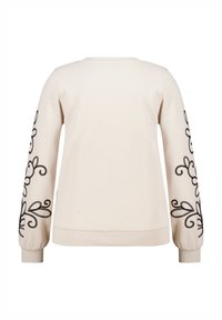 Sweatshirt beige clair à manches longues avec des motifs floraux noirs brodés sur les bras et des poignets et un ourlet côtelés.