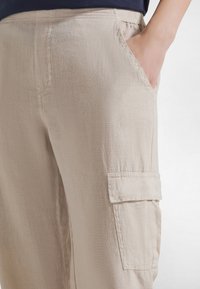 Beiget väriset cargo-housut, joissa on teksturoitu kangas, sivutasku ja rento istuvuus. Vyötärönauha on joustava mukavuutta varten.