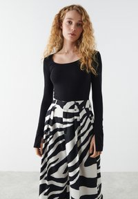 Zwart lange mouw top gecombineerd met hoge taillebroek met een gedurfde zwart-wit zebraprint en plooidetails.