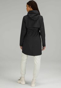 Svart regnjacka med huva, åtdragen midja och långa ärmar. Slät yta med en minimalistisk design och ingen synlig hårdvara.