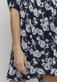 Námořnické šaty s bílými květinovými vzory, lehká látka, krátké nabírané rukávy a nabíraný korzet, s uvolněným střihem a jemnou strukturou.