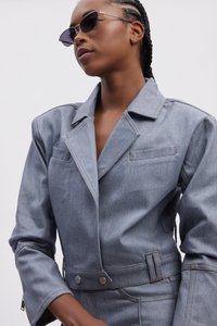 Jeansjacka i ljusblått med strukturerade slag, två bröstfickor och kontrasterande sömmar; modell som bär smala solglasögon.