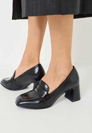 Schwarze Leder-High-Heels mit eckiger Zehenpartie und niedrigem Ausschnitt. Sie haben eine glänzende Oberfläche und einen klobigen, kantigen Absatz.