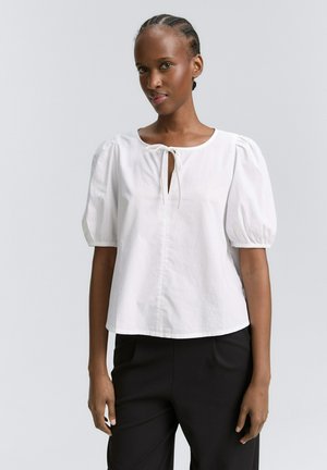 Blouse en coton blanc avec des manches bouffantes, un col rond et un détail en forme de trou de clé à l'avant. Texture lisse, coupe décontractée, tombant à la taille.