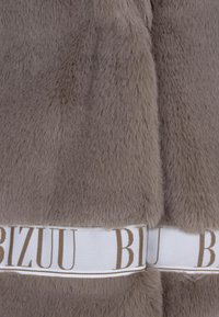 Nepvacht stof in zacht grijs met een gladde textuur. Bevat een witte merkband met lichtbruine letters in het midden.