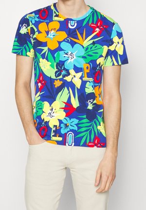 Kortærmet blå t-shirt med et levende blomsterprint i gult, rødt og grønt, med farverige tekstaccents i forskellige stilarter.