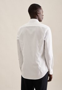 Camicia bianca con bottoni, dal tessuto liscio, colletto classico e maniche lunghe. Vestibilità sartoriale con orlo curvo e cuciture a contrasto delicate.