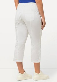 Pantalons blancs coupés avec une texture lisse, dotés de deux poches arrière et de coutures latérales. Associés à des baskets blanches pour un look décontracté.