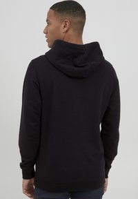 Felpa nera con cappuccio caratterizzata da un cordino, polsini a costine e una texture morbida. Il retro presenta un design semplice e lineare senza decorazioni.