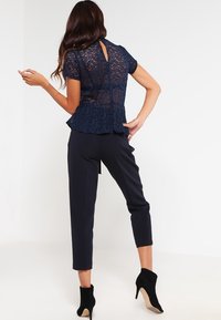 Marinblå spetsblus med korta ärmar och nyckelhålsrygg, matchad med skräddarsydda marinblå byxor och svarta högklackade ankelstövlar.