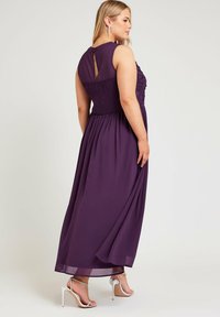 Pitkä violetti mekko, jossa on smokkivuori, hihaton muotoilu ja avara selkäosa, yhdistettynä hopeisiin korkeakorkoisiin sandaaleihin.