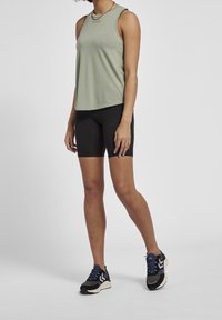 Ljusgrön ärmlös topp, svarta cykelshorts och svarta sneakers med blå accenter. Slät tyg, figurnära design och minimalistisk stil.