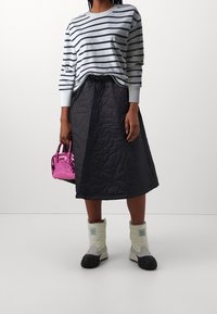 Camisa de manga larga a rayas, falda acolchada negra, botas blancas con detalles negros y un pequeño bolso rosa brillante. Detalles de la tela texturizada visibles.