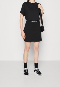 Černé krátké tričko a miniskirt s logem Calvin Klein Jeans v pase. Doplňeno černými teniskami Adidas a černými ponožkami.