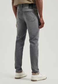 Szürke farmernadrág, slim fit fazonnal, klasszikus öt zsebes dizájnnal, finom kopással és márka címkével a derékon.