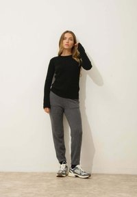 Czarny prążkowany sweter, szare dresy i wielokolorowe sneakersy. Strój charakteryzuje się luźnym krojem i teksturowanymi materiałami.