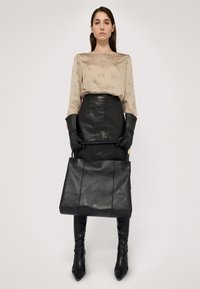 Czarna skórzana torba typu tote o zarysie strukturalnym, z górnymi uchwytami i subtelnym złotym logo. Skórzana spódnica o teksturze w kolorze czarnym oraz beżowa bluzka z nadrukami.
