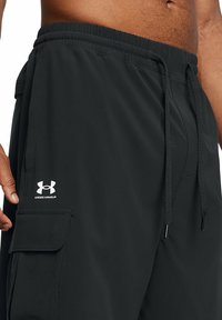 Svarta sportshorts med resårmidja och snörning, sidoficka och en vit Under Armour-logotyp nära nederkanten.